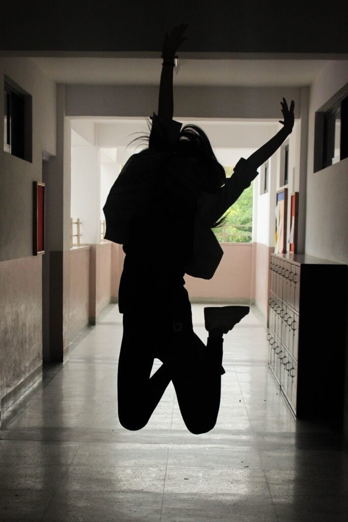 jeune fille dans le hall d'un couloir de lycée, sautant les bras en l'air 
au milieu un bouton indiquant intervention scolaire et ears